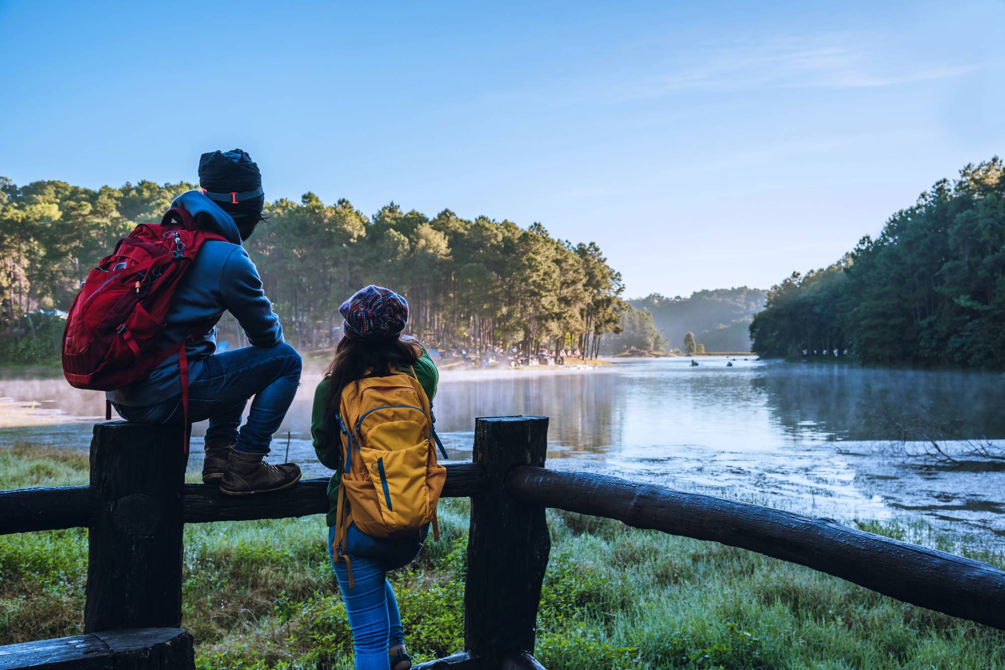 Two backpackers relaxing on a fence, looking at a lake surrounded by trees; bamboo forest for climate change